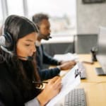 woman with headset holding a clipboard and taking notes